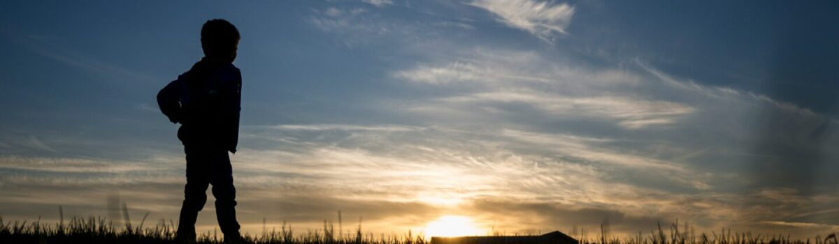 Kind in Silhouette sieht in die Ferne und betrachtet den Sonnenaufgang