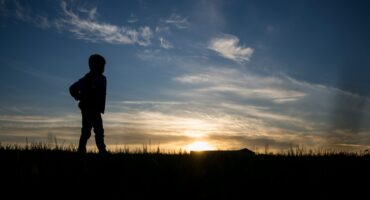 Kind in Silhouette sieht in die Ferne und betrachtet den Sonnenaufgang
